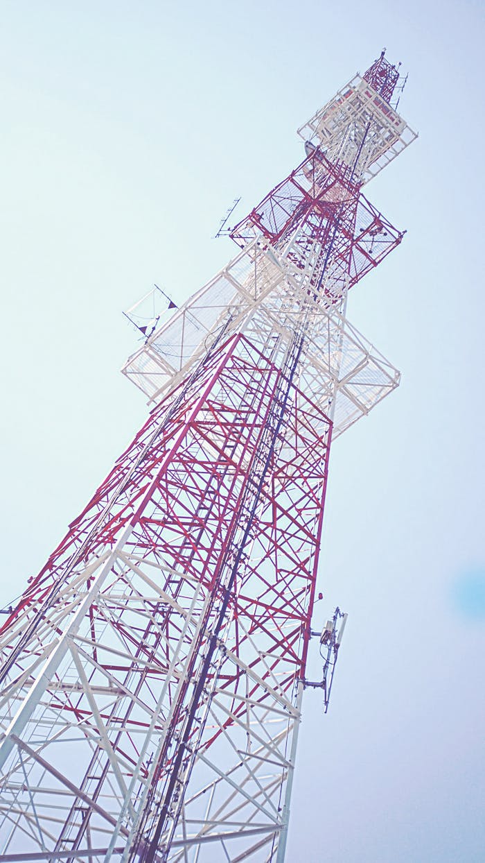Low angle view of a red and white communication tower against a clear blue sky, capturing modern technology.